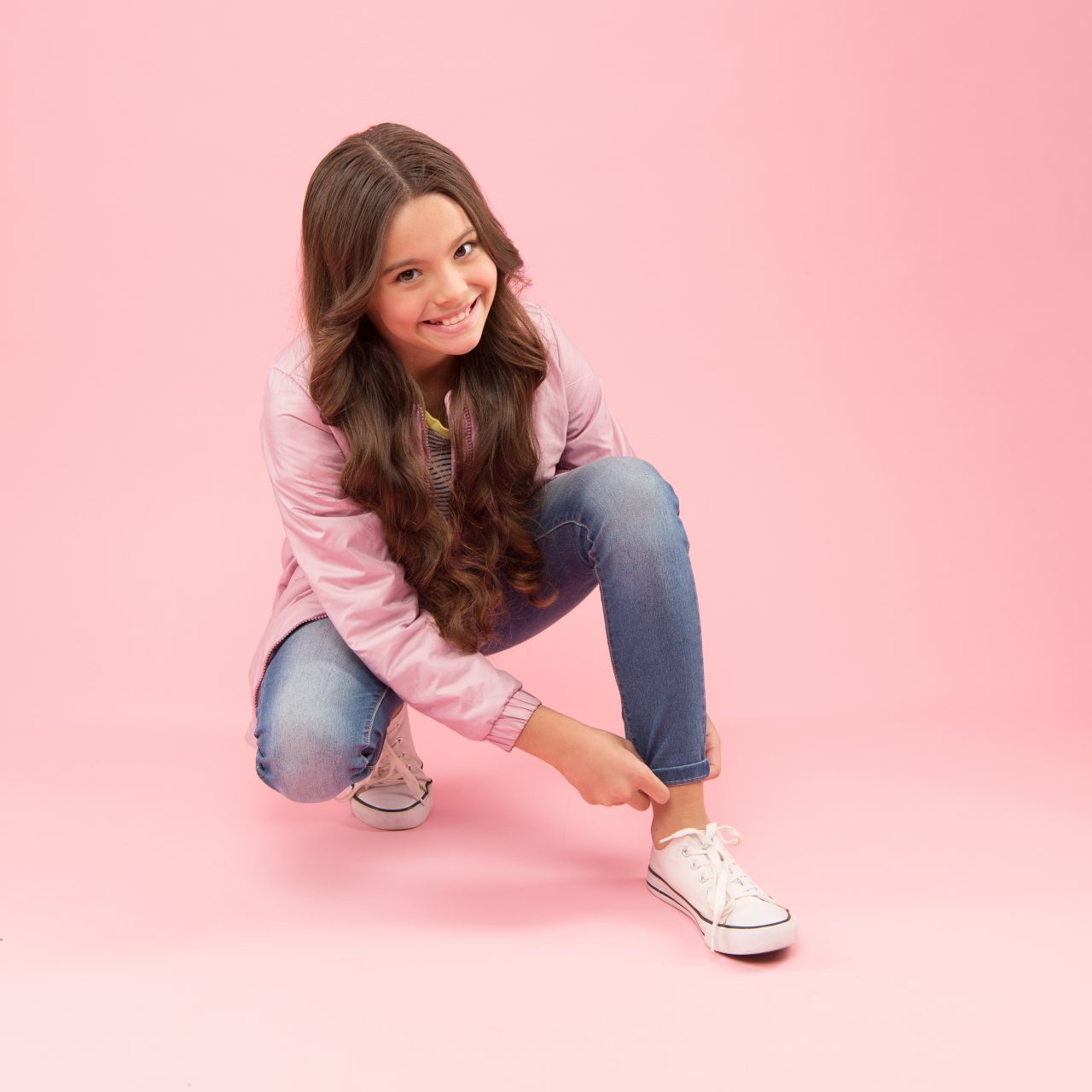 Adorable and stylish. Happy child fix jeans on pink background. Beauty look of little girl child. Fashion child smile in casual style. Cute small child smiling with long curly hair.